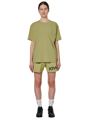 Person iført oversize T-shirt i olivengrøn og matchende shorts med mørkegrønt logo, hvide sokker og sorte sneakers, stående med fronten mod kameraet.