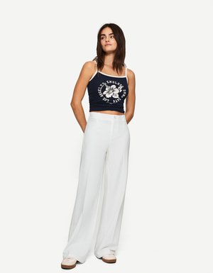 Top scurt navy cu grafică florală albă; asortat cu pantaloni albi, cu talie înaltă și croială lejeră, și tenisi bej.
