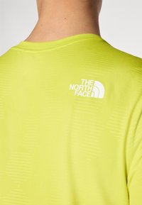 Camiseta atlética de manga corta, de un brillante color amarillo, con un patrón texturizado. Presenta un logo blanco en la parte superior de la espalda. Ligera, con escote redondo.