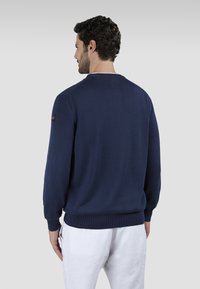 Maglione girocollo blu navy con polsini e orlo a costine. Tessuto liscio, design minimalista, patch logo sulla manica sinistra. Vestibilità casual.