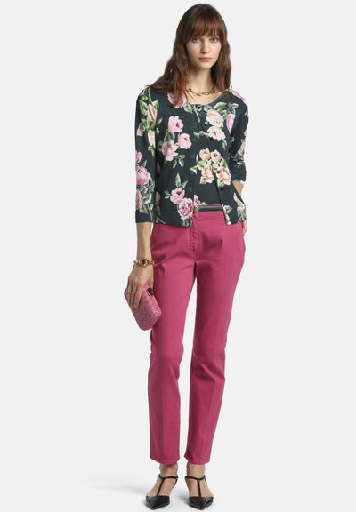 Cardigan noir à motif floral avec des fleurs roses et beiges, associé à un pantalon rose ajusté. Accentué par une pochette rose texturée et des talons noirs.