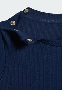 Tmavomodrý vrúbkovaný top s okrúhlym výstrihom, s striebornými patentkami na ramene na zapínanie a zdobenie. Hladká textúra.