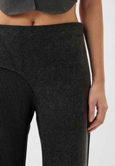 Black high-waisted trousers with a textured finish, featuring pinstripe pattern on one side and a curved cut-out detail.