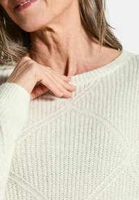 Cremfarbener gestrickter Pullover mit strukturiertem Rippenmuster und geometrischen Akzenten. Rundhalsausschnitt und lockere Passform.