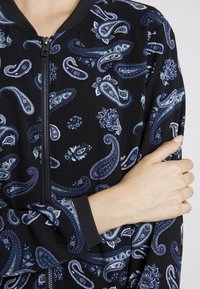 Svart bomberjacka med paisleymönster i blå och gröna nyanser, ribbade ärmslut och dragkedja fram. Texturerat tyg.