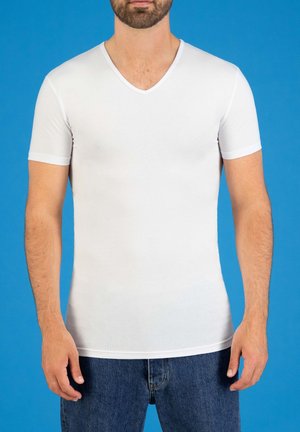 Witte korte mouwen V-hals t-shirt van een lichtgewicht, gladde stof, aansluitend ontwerp, gecombineerd met blauwe denim jeans tegen een blauwe achtergrond.