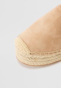 Bež zamsheva espadrila z delikatno prejo jute na prstih in ob robu podplata, z okroglo sprednjo stranjo in ravnim dnom.