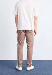 Ljusbeige t-shirt med en avslappnad passform, tillsammans med bruna sweatpants med vita sidon stripes och vita sneakers. Enkel design, mjuk textur.