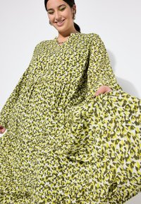 Vestido maxi floral en tonos verdes y amarillos, con un corte relajado, mangas largas y cintura fruncida, hecho de una tela ligera.