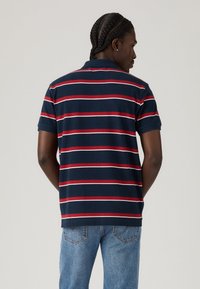 Ναυτικό polo μπλουζάκι με κόκκινες και λευκές οριζόντιες ρίγες. Κοντά μανίκια και γιακά, κατασκευασμένο από μαλακό ύφασμα. Φοριέται με ανοιχτούς μπλε τζιν.