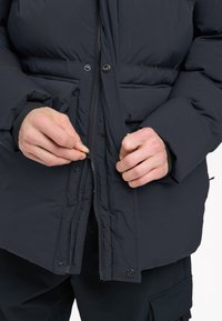 Schwarze Daunenjacke mit durchgehendem Reißverschluss, hoher Kragen und Knopfdetails. Der Stoff wirkt glatt und isolierend, ideal für kaltes Wetter.