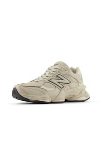 Baskets beiges avec tige en mesh et daim, arborant un logo "N" foncé proéminent, un design épuré, des accents texturés et une semelle en caoutchouc noire.