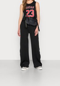 Musta hihaton paita, jossa punaisella "Jordan" ja "23", yhdistettynä löysiin mustiin housuihin ja kuvioituun vyölaukkuun. Asun täydentävät valkoiset lenkkarit.