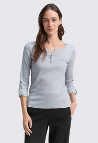 Light gray long-sleeve top with a henley neck and three buttons. Soft, textured fabric with rolled-up sleeves and a fitted design.