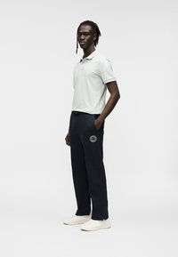 Ανοιχτό πράσινο πόλο με κοντά μανίκια, συνδυασμένο με σκούρο μπλε παντελόνι που έχει κεντητό κυκλικό σχέδιο και ανοιχτόχρωμα αθλητικά παπούτσια.