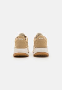 Beige semskede sneakers med en teksturert kropp, hvit merkevarelogo på hælen, og en gummisåle med et subtilt mønster.