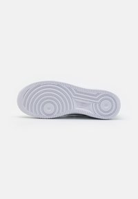 Semelle d'une chaussure blanche Nike avec des motifs circulaires et le logo Nike au centre sur un fond uni.