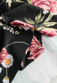 Tejido floral con grandes rosas rosas y margaritas blancas sobre un fondo negro, combinando con una ligera textura floral en el reverso.