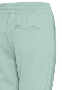 Ljusgröna träningsoveraller med elastisk midja, som har en bakficka och en slät textur. Designen är enkel och kroppsnära.