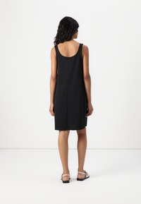 Rochie neagră fără mâneci, cu decolteu rotund la spate, croi drept, până la genunchi, dintr-un material neted. Complementată cu sandale simple, plate.