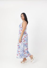 Robe maxi avec un imprimé floral en bleu, rose et blanc. Tissu léger, design à encolure halter et silhouette fluide. Portée avec des talons.