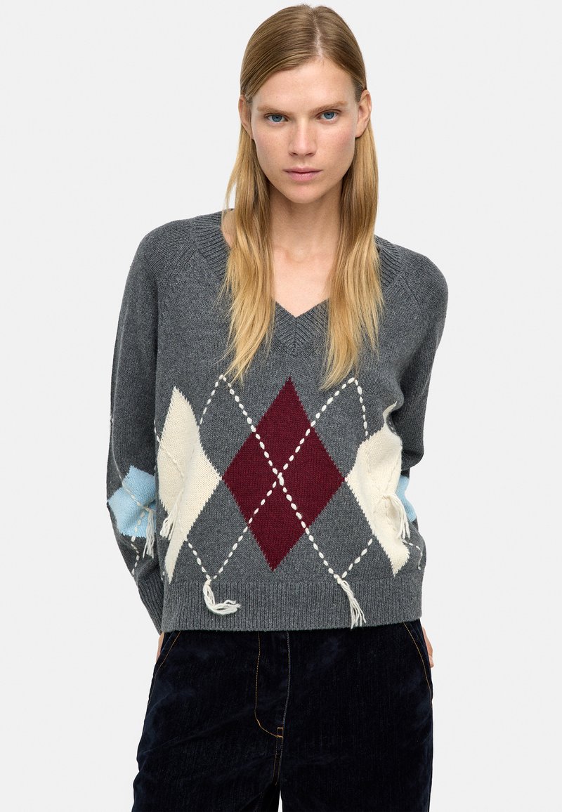 Szary sweter z dekoltem w serek, zdobiony diamentowym wzorem w kolorach burgundu, kremu i jasnoniebieskiego, z postrzępionymi brzegami. Dzianinowa struktura o luźnym kroju.