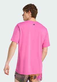 Lys pink kortærmet t-shirt lavet af glat stof, med rund halsudskæring og en lille sort logo detalje på den øverste del af ryggen.