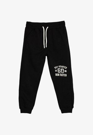 Zwarte sweatpants met een trekkoord in de taille, zijzakken en geribbelde manchetten, met witte tekst: "GA VAN START 1986 LOOP SNELLER."