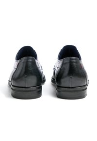 Schwarze Lederschuhe mit glatter Oberfläche, abgerundeter Zehenpartie, niedrigem Absatz und gesteppten Akzenten. Die Rückseite hat ein minimalistisches Design mit dezentem Branding.