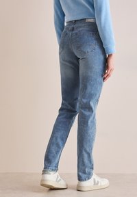 Jasnoniebieskie dżinsy o slim fit, z pięcioma kieszeniami i subtelnym przetarciem na nogawkach, w połączeniu z białymi trampkami.