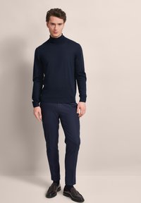 Navy-Farbenes Rollkragensweatshirt aus weichem Stoff, kombiniert mit maßgeschneiderten navyfarbenen Hosen und dunklen Slippern. Es zeichnet sich durch eine figurbetonte Passform und gerippte Bündchen aus.