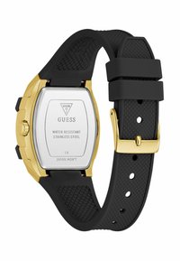 Cinturino in gomma nera con cassa in oro e argento. Sul retro sono visibili il marchio e le specifiche: "Guess," resistente all'acqua, acciaio inossidabile.