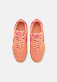 Paire de baskets Nike pêche et rose avec lacets, vue de dessus, montrant la languette marquée et la semelle en gomme sur fond blanc.