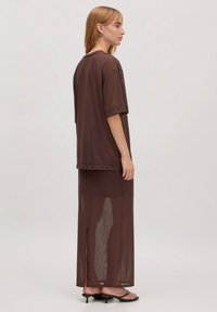 Bruine doorzichtige top gecombineerd met een bijpassende lange rok met een split aan de zijkant. De stof is lichtgewicht met een gladde textuur en een relaxte pasvorm.