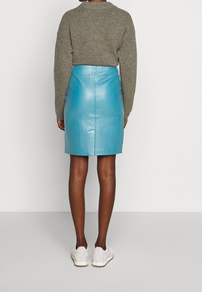 Getailleerde blauwe leren rok met een gladde textuur, hoge taille en subtiele naaddetails, gecombineerd met een grijze gebreide trui en witte sneakers.