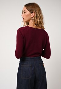 Maglione bordeaux in maglia con scollo rotondo, abbinato a pantaloni in denim scuro a vita alta con cuciture a contrasto e tasche posteriori.