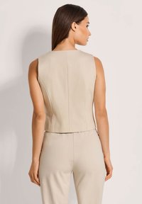 Beige, ärmelloses Top mit strukturiertem Design, das einen hohen Ausschnitt und saubere Nähte aufweist. Glatte Textur, cropped Länge.