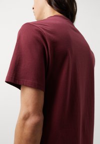Camiseta de algodón burdeos con mangas cortas y cuello redondo, que muestra una textura suave y un detalle de costura limpia en el dobladillo.
