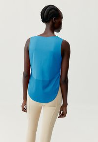 Blå, ermeløs topp med avrundet kant og en gjennomsiktig panel. Kombinert med tettsittende beige leggings som fremhever en glatt tekstur.