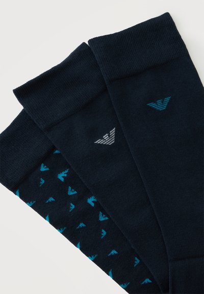 Trois paires de chaussettes noires, une avec un petit motif de logos bleus, deux avec un logo bleu et blanc unique près du bord-côte, disposées côte à côte.