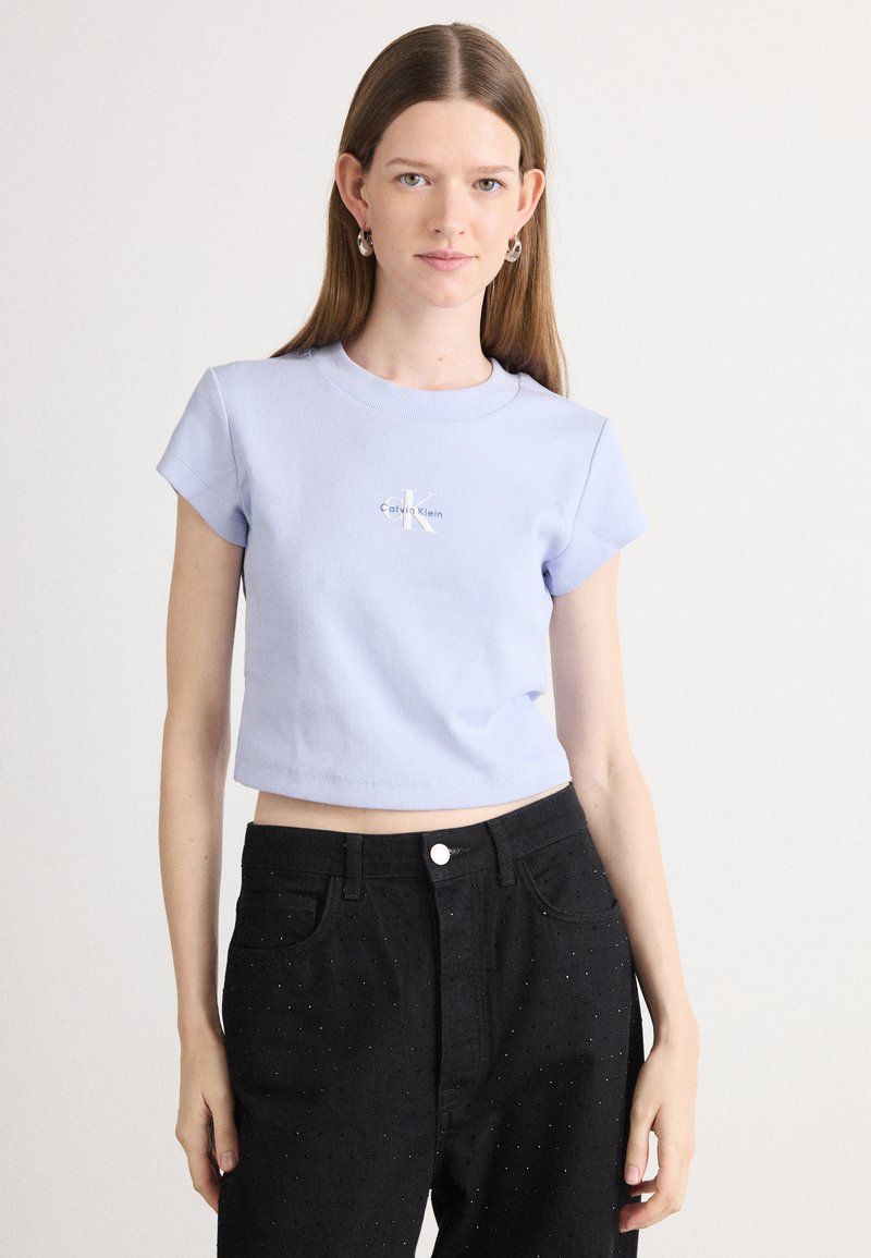 Jasnoniebieski krótki t-shirt z krótkimi rękawami i okrągłym dekoltem, z białym logo. Połączony z czarnymi dżinsami ozdobionymi błyszczącymi kropkami.