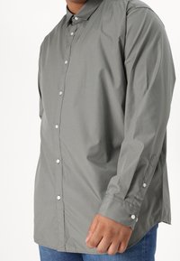 Camisa gris de botones con cuello puntiagudo, mangas largas y botones blancos. Tejido suave con un ajuste ligeramente holgado. Combínala con jeans de mezclilla.