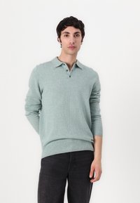 Světle zelený svetr s polo límcem, třemi předními knoflíky, žebrovanými manžetami a lemem. Nosit s tmavými džíny, jednoduchý design a měkká textura.
