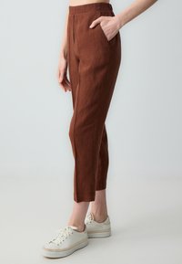 Czekoladowe lniane spodnie o dopasowanym kroju, wysokim stanie, bocznych kieszeniach i skróconej długości. Połączone z białymi sneakersami, prezentując casualowy wygląd.