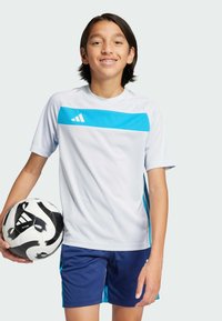 Camiseta deportiva blanca con acentos azules, de manga corta; combinada con pantalones cortos azul marino. Niño sosteniendo un balón de fútbol blanco y negro.