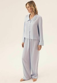 Jasnoniebieski komplet piżamowy z kołnierzykiem, składający się z zapinanej na guziki koszuli i spodni o szerokich nogawkach. Wykonany z gładkiego materiału, luźny krój i mankiety.
