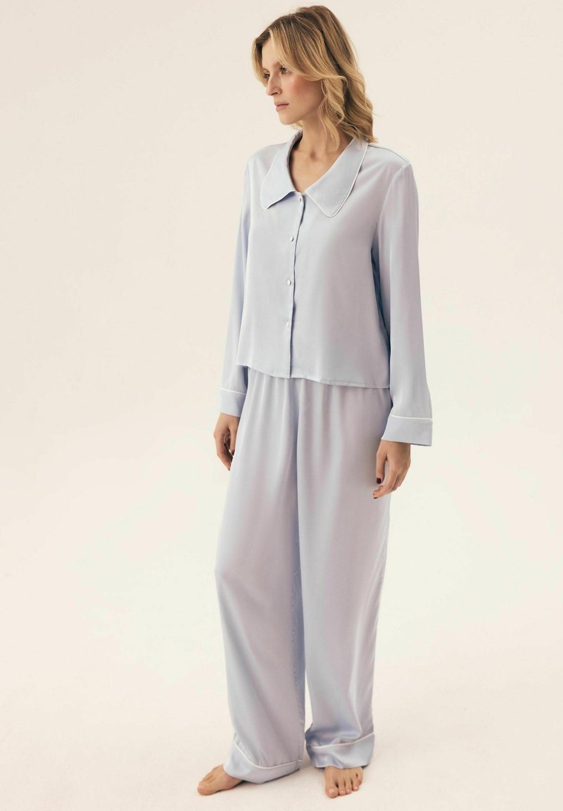 Jasnoniebieski komplet piżamowy z kołnierzykiem, składający się z zapinanej na guziki koszuli i spodni o szerokich nogawkach. Wykonany z gładkiego materiału, luźny krój i mankiety.