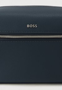 Mørkeblå læderkosmetikpose med en struktureret overflade, der har en sølvlynlås og præget mærkelogo på forsiden.