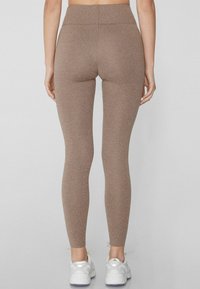 Leggings marrones elásticos con cintura alta, diseño sin costuras y una textura suave, combinados con zapatillas deportivas blancas.