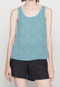 Top senza maniche blu chiaro con pois neri, realizzato in un tessuto liscio, caratterizzato da un colletto rotondo e una vestibilità ampia. Abbinato a pantaloni corti scuri.